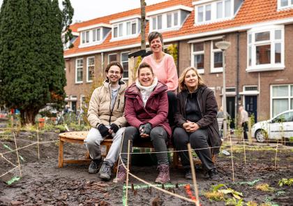 Vier bestuursleden van buurtvereniging De Triangel zitten op het bankje onder de pas geplante boom.